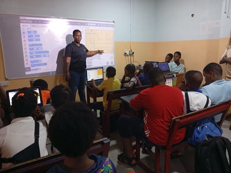 An instructor teaching block-based coding to a full classroom, with the code projected on screen
