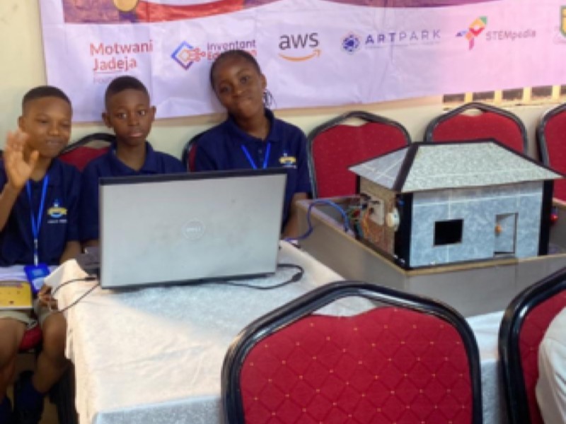 Three students presenting a model building project they constructed alongside their laptop work
